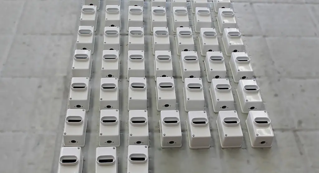 Mehrere weiße, lackierte Metallgehäuse in Reihung auf einem Werkboden.