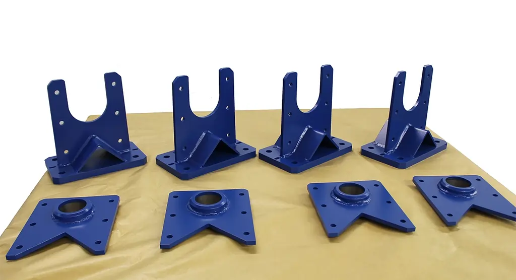 Acht blau lackierte Metallbauteile auf einer Werkbank, bereit zur weiteren Montage.
