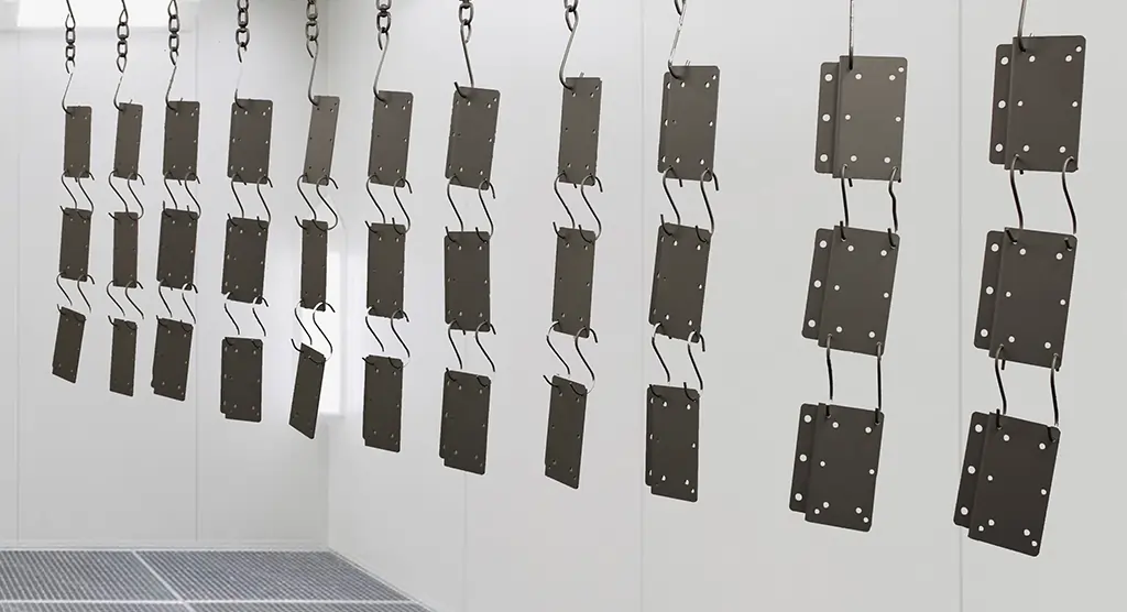 Mehrere lackierte Metallplatten hängen in einer Kabine zum Trocknen nach der Pulverbeschichtung.