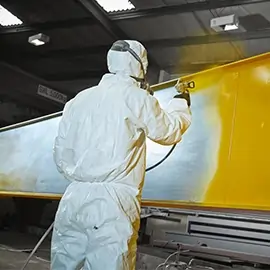 Arbeiter in Schutzkleidung beim Lackieren einer großen Metallplatte in Gelb.